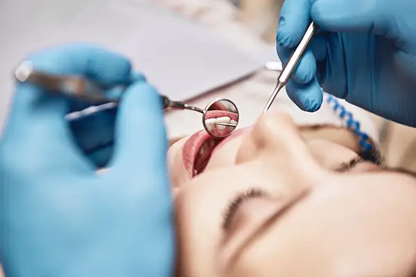 A dentist performing an oral examination on a patient using dental tools while the patient reclines in the chair.